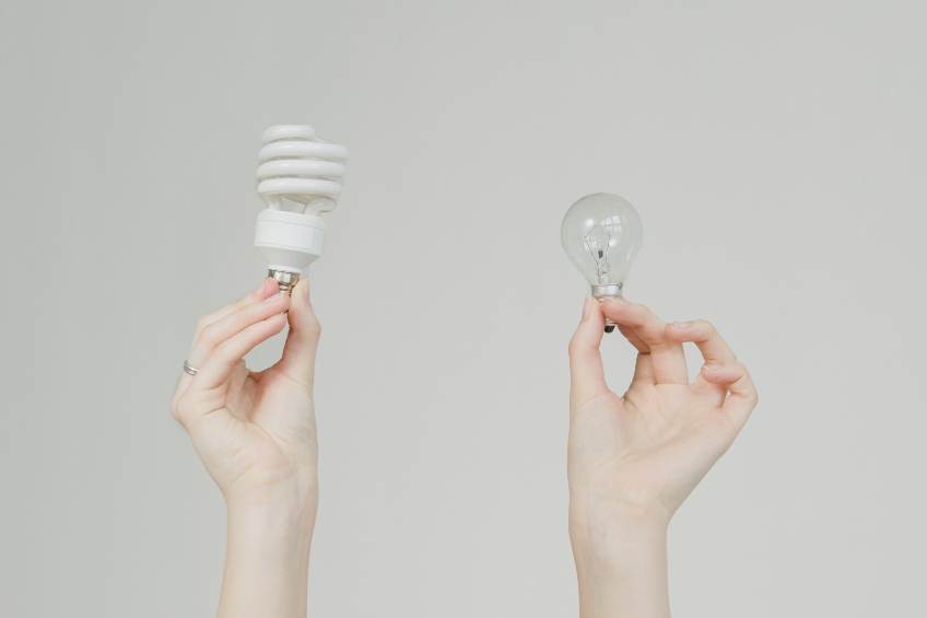 One hand holding up an energy efficient lightbulb, one hand holding an incandescent light bulb.